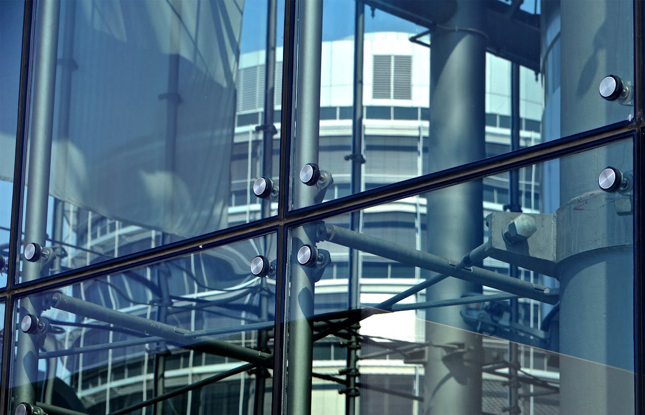 Close-up of a modern glass building facade reflecting industrial structures.